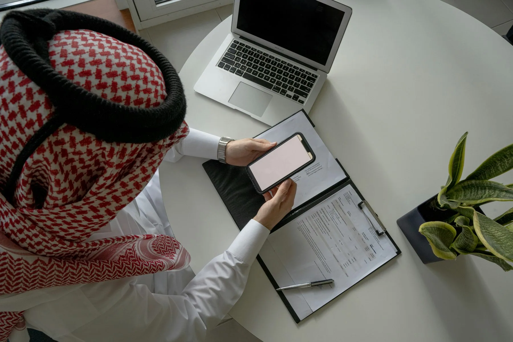 Saudi professional reviewing compliance documents beside a laptop